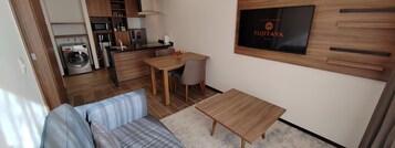 Una habitación de hotel compacta con kitchenette, un sofá, una mesita y un televisor montado en la pared.