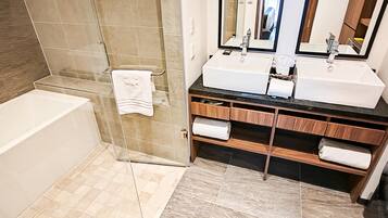 A bathroom with a bathtub, two sinks, a mirror, and a shower area.