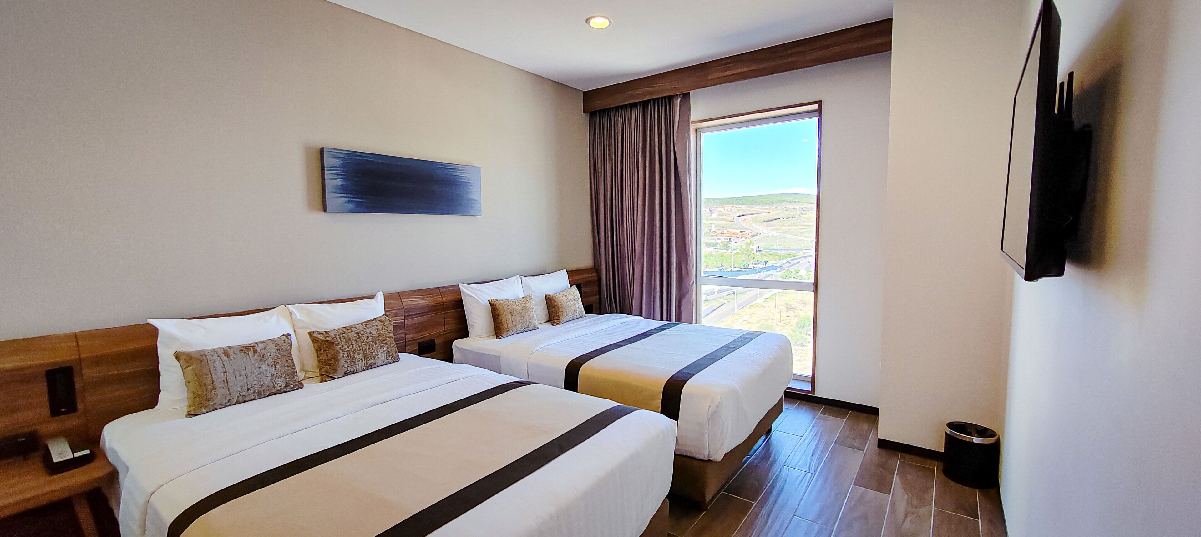 A hotel room with two beds, a large window, a flat-screen TV, and a painting on the wall.
