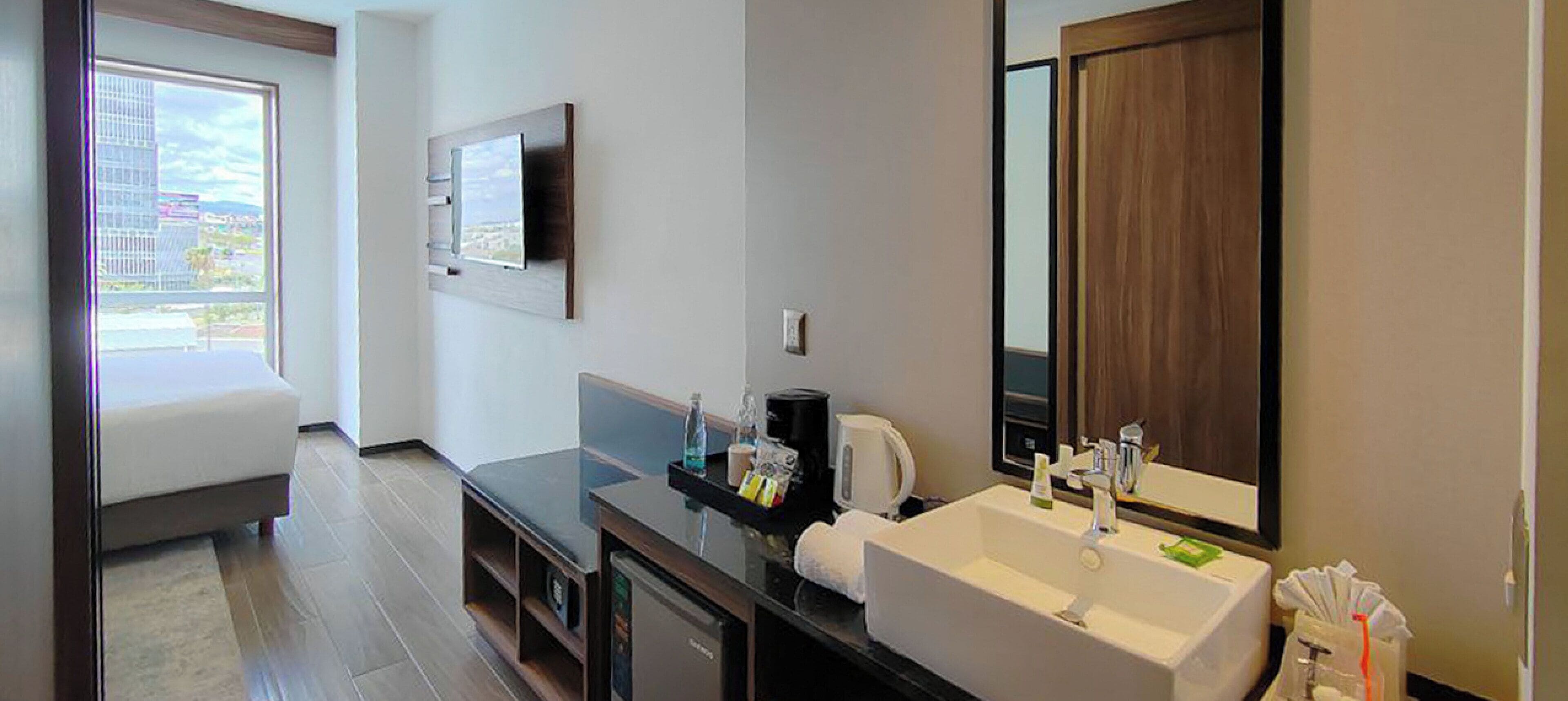 Un baño moderno con un lavamanos grande, un espejo y un televisor montado en la pared.