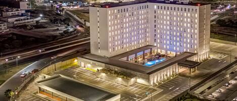 A large, modern hotel with a central courtyard, multiple parking levels, and a prominent rooftop pool.