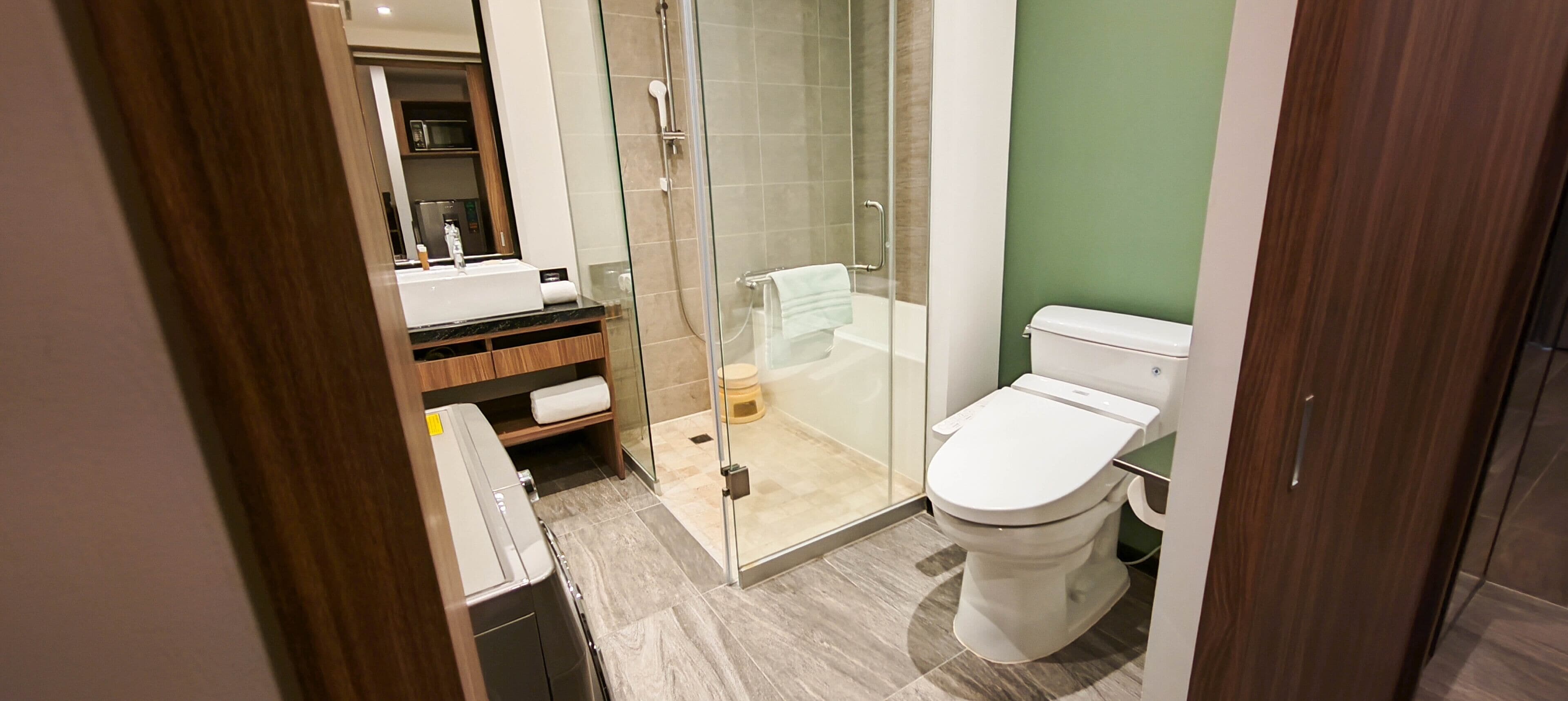 Un baño moderno con ducha de vidrio, inodoro blanco y tocador de madera con lavamanos.