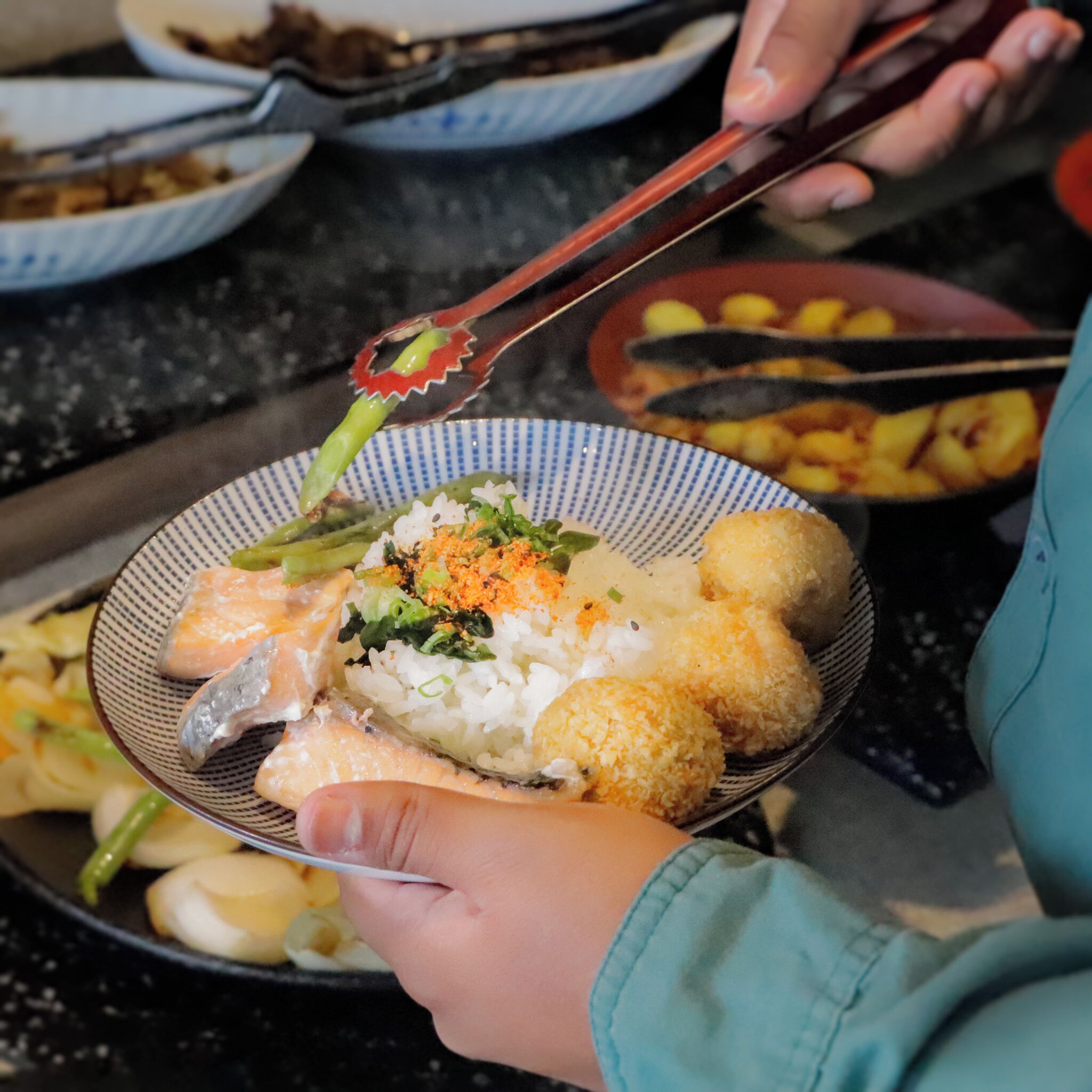 Uma pessoa segurando uma tigela com diversos alimentos, incluindo arroz, legumes e possivelmente frutos do mar.