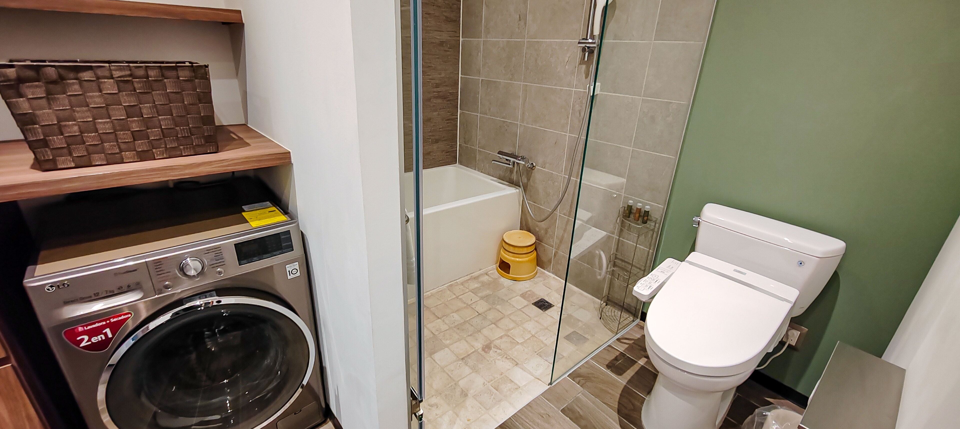 Un baño pequeño con lavadora, cabina de ducha de vidrio y retrete.