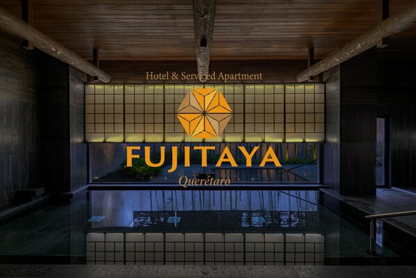 A modern hotel lobby with a large sign reading "FUJITAYA Querétaro" and a wooden ceiling.