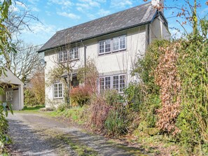Une maison à deux étages avec une allée en gravier et une végétation luxuriante tout autour.