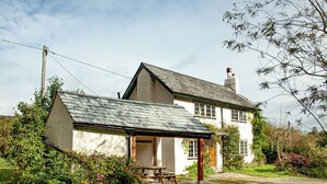 Ein traditionelles Haus mit geneigtem Dach, einem sichtbaren Schornstein und einem kleinen Garten mit einem Picknicktisch.