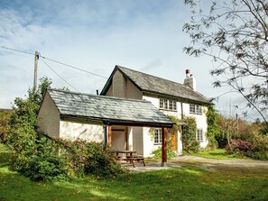 Een traditioneel huis met een schuin dak, een opvallende schoorsteen en een kleine tuin met een picknicktafel.