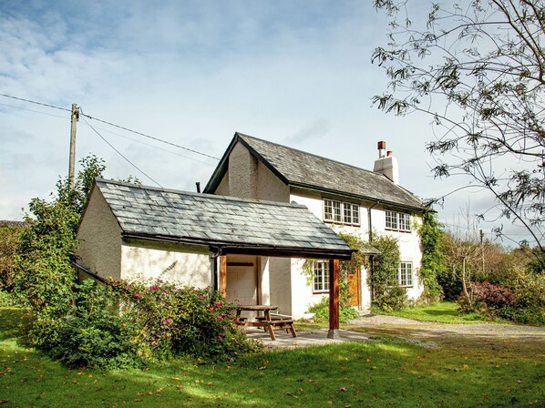 A traditional house with a sloped roof, a visible chimney, and a small garden area with a picnic table.