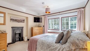 Ein Schlafzimmer mit Bett, Fernseher, Kamin, einem Fenster mit Vorhängen und einer Deckenleuchte.