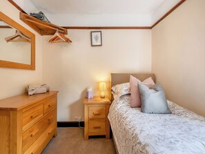 Une chambre à coucher avec une commode en bois, une table de chevet avec une lampe, un lit avec une literie à motifs floraux et un miroir fixé au mur.