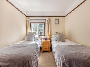 Une chambre avec deux lits simples, une table de chevet en bois, une fenêtre avec des rideaux et un tableau encadré au mur.