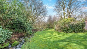 Eine natürliche Landschaft mit einem Bach, einer grasbewachsenen Fläche und dichter Strauchvegetation.