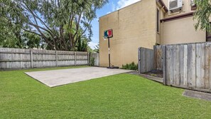 A backyard with a basketball hoop, a wooden fence, and a concrete patio.