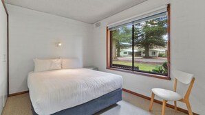 A bedroom with a bed, a chair, a window with a view of a house and trees, and a wall-mounted light. - Perfect for your beach holiday, you are only a stone's throw to the Port Fairy East Beach (Port Fairy)