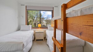 A bedroom with two single beds, a nightstand with a lamp, and a window with a view of trees. - Perfect for your beach holiday, you are only a stone's throw to the Port Fairy East Beach (Port Fairy)