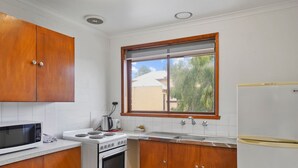 A compact kitchen with wooden cabinets, a microwave, stove, sink, and a refrigerator. - Perfect for your beach holiday, you are only a stone's throw to the Port Fairy East Beach (Port Fairy)