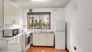 Une cuisine de taille réduite avec des meubles blancs, un four à micro-ondes, une cuisinière et un réfrigérateur.