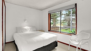 Une chambre à coucher comprenant un lit, une table de chevet, une chaise et une fenêtre donnant sur des arbres et une maison.