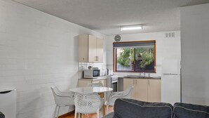 A compact kitchen with white cabinets, a microwave, an oven, and a sink. There is a dining area with a white table and chairs. - Perfect for your beach holiday, you are only a stone's throw to the Port Fairy East Beach (Port Fairy)