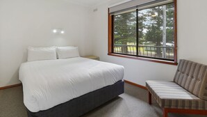 A bedroom with a bed, a chair, a window with a view of trees, and a ceiling light. - Perfect for your beach holiday, you are only a stone's throw to the Port Fairy East Beach (PORT FAIRY)