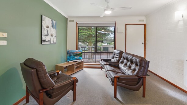 A living room with a sofa, armchair, TV, and artwork on the wall. - Perfect for your beach holiday, you are only a stone's throw to the Port Fairy East Beach (PORT FAIRY)