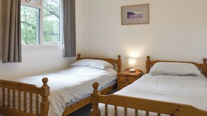 Une chambre avec deux lits en bois, une table de chevet avec une lampe, une fenêtre avec des rideaux et un tableau encadré au mur.