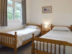 A room with two wooden beds, a nightstand with a lamp, a window with curtains, and a framed picture on the wall. - 2 bedroom accommodation in Mount Hawke, near Redruth (Mount Hawke, near Redruth)