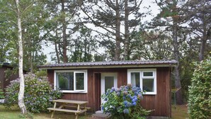 Une petite cabane en bois avec une seule fenêtre, une porte et un banc à l’extérieur.