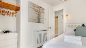 Une chambre à coucher avec un lit, une commode blanche, un porte-manteau, un radiateur et un tableau accroché au mur.
