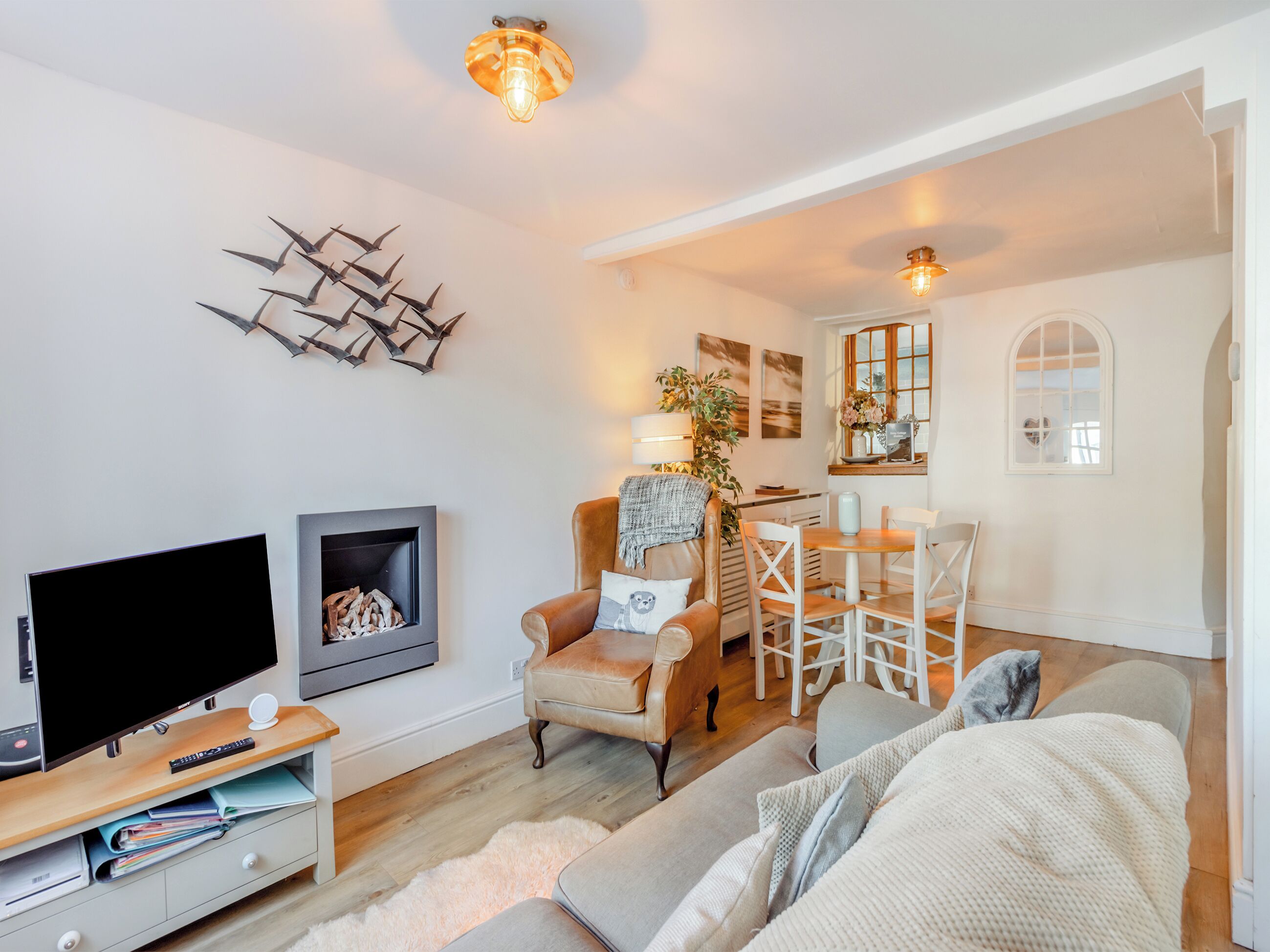 A modern living room with a flat-screen TV, a fireplace, a leather armchair, a dining table with chairs, and a cozy sofa.