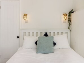 A bedroom with a white bed, two wall-mounted lights, and a door.
