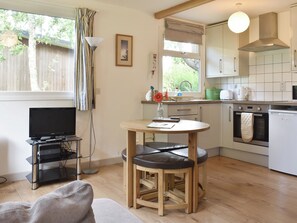 A compact kitchen with a dining area, a television, and a window with curtains.