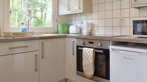 A modern kitchen with white cabinets, a stainless steel oven, and a window with a view of trees. - 2 bedroom accommodation in Mount Hawke, near Redruth (Mount Hawke, near Redruth)