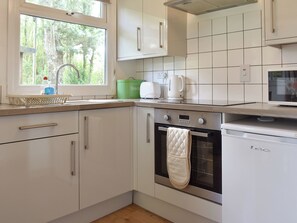 Une cuisine moderne avec des armoires blanches, un four en acier inoxydable et une fenêtre donnant sur les arbres.