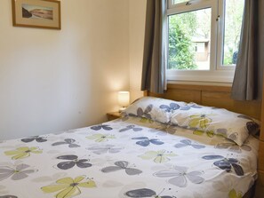 A bedroom with a bed, a bedside lamp, a window with curtains, and a framed picture on the wall.