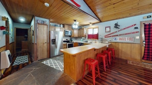 A kitchen with wooden cabinets, a stainless steel refrigerator, a microwave, and a bar area with red stools.