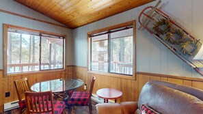 A room with a glass table, wooden chairs, a leather sofa, and a wooden ceiling.