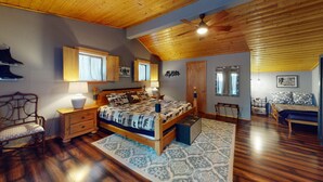 Une chambre à coucher avec un plafond en bois, un lit avec une literie à motifs, une table de chevet, une chaise et une petite table d’appoint.