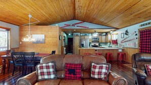 L’intérieur chaleureux d’un chalet avec un plafond en bois, un coin repas, un salon doté d’un canapé en cuir et une cuisine avec des meubles en bois.