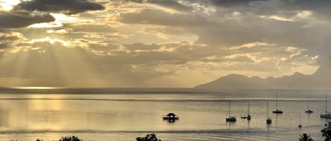 A coastal scene with boats, a clear sky, and a mountain in the distance.
