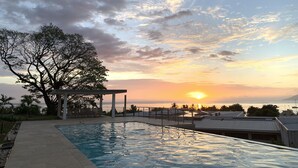Une piscine avec vue sur le coucher de soleil et un arbre.