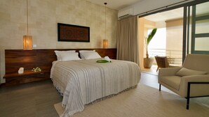 Une chambre d’hôtel moderne avec un grand lit, une tête de lit en bois, une table de chevet ornée d’un vase de fleurs, une chaise et une vue sur l’extérieur grâce à une porte coulissante.