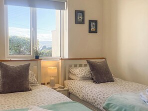 Un dormitorio con dos camas, una ventana con vistas, una lámpara de noche y dos cuadros en la pared.