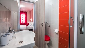 Een moderne badkamer met een witte wastafel, toilet in het rood en een douchehoek.