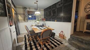 A dining area with a checkered rug, wooden table, wicker chairs, and a hanging light fixture.
