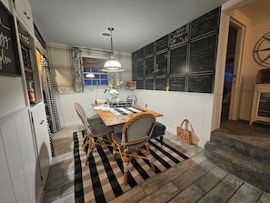 A dining area with a checkered rug, wooden table, wicker chairs, and a hanging light fixture.