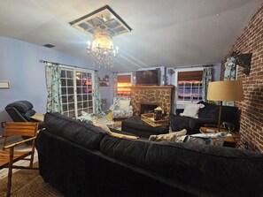 A living room with a stone fireplace, a black sofa, a wooden chair, and a television on the wall.