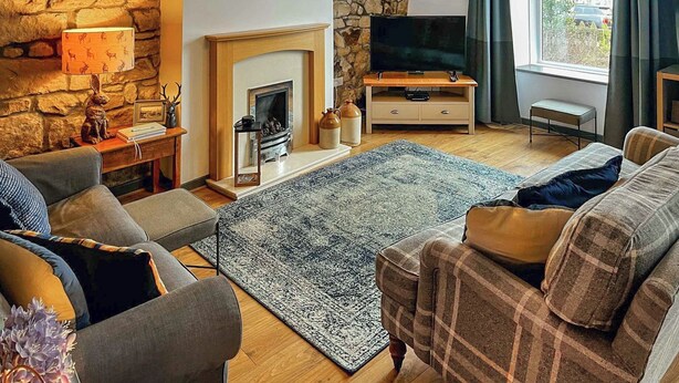 Un salon chaleureux avec un mur en pierre, une cheminée, un téléviseur et des fauteuils confortables.