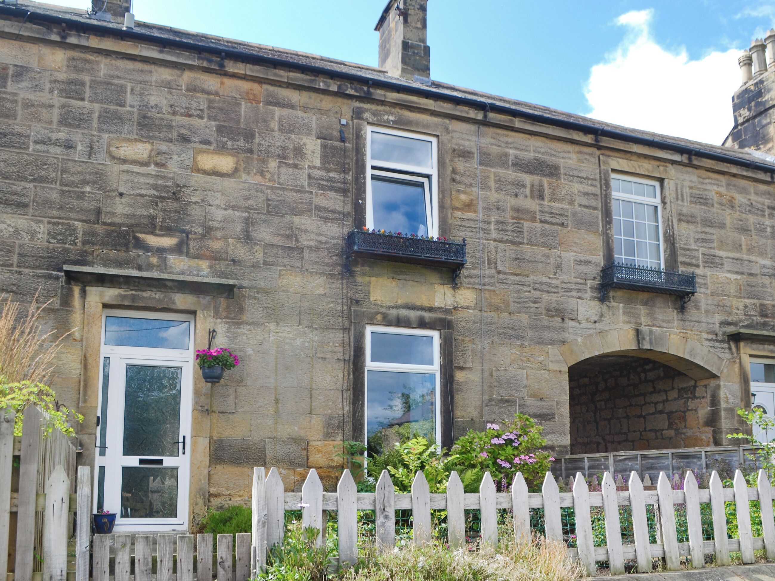 A stone building with three windows, a white picket fence, and a flower pot on the left.